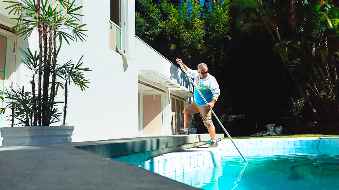 Piscineiro realizando limpeza em piscina residencial