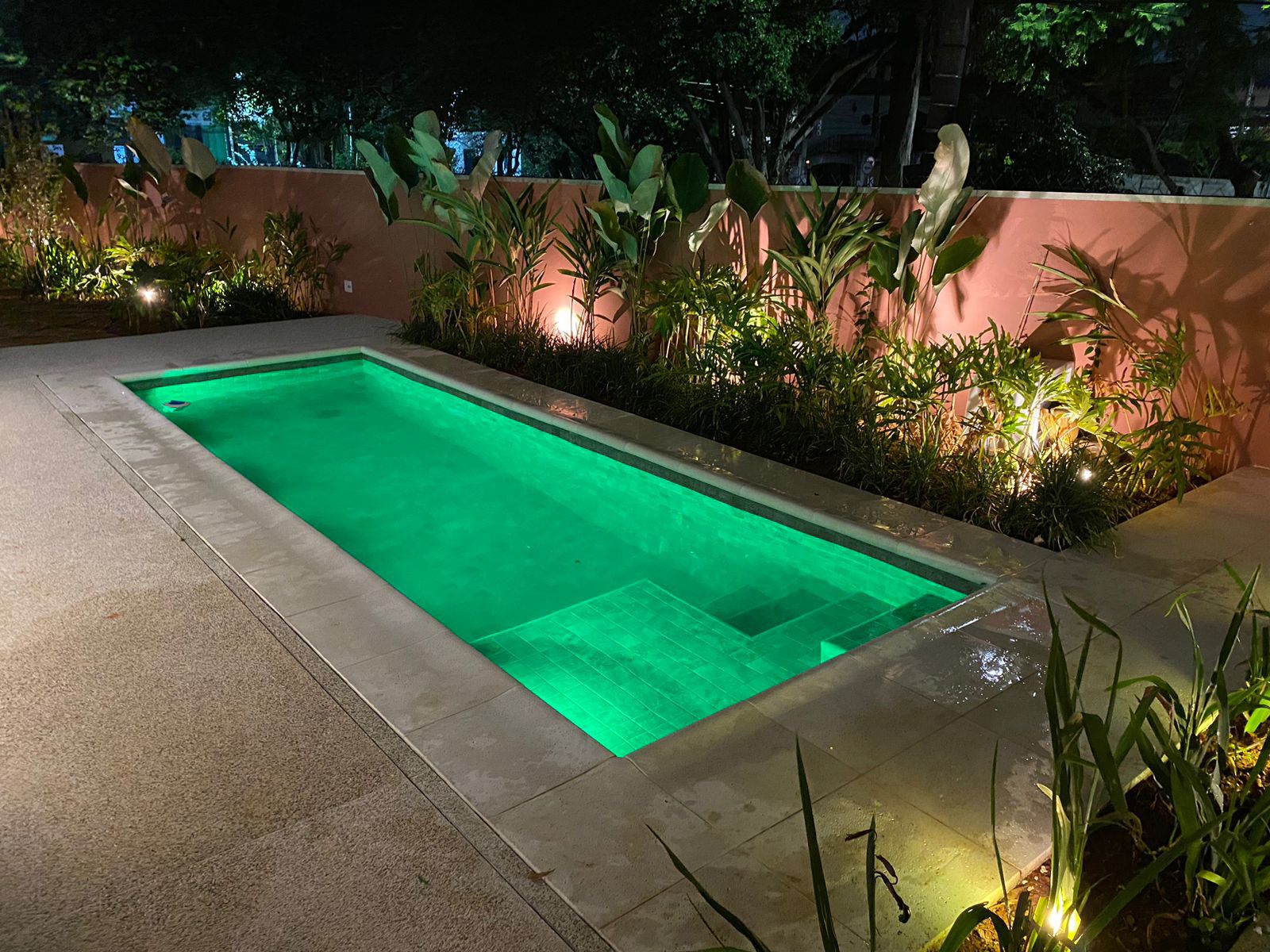 Piscina residencial finalizada com iluminação subaquática verde e paisagismo
